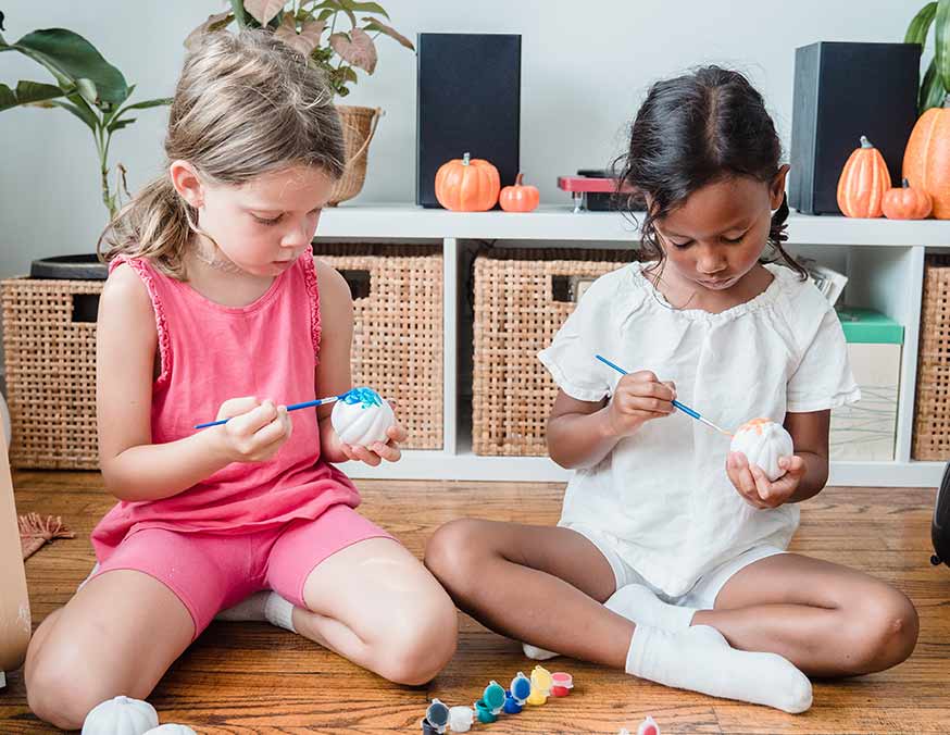 Two girls painting small pumpkins