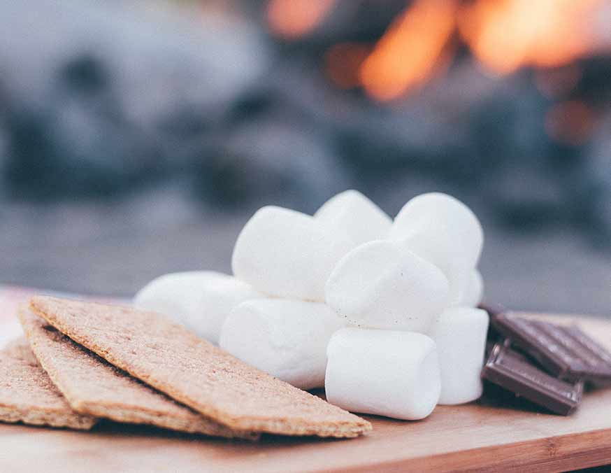 Graham crackers, marshmallows, and chocolate with fire in the background